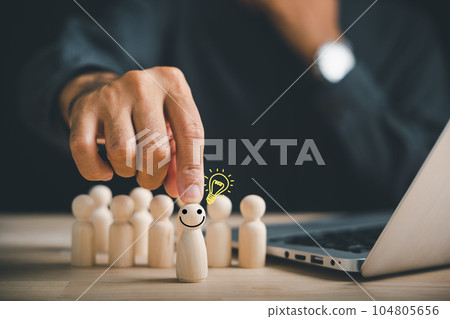 A happy wooden person figure holds a light bulb, embodying creative thinking and inspiration. Leadership and teamwork create an environment where ideas are shared and new concepts are born. 104805656