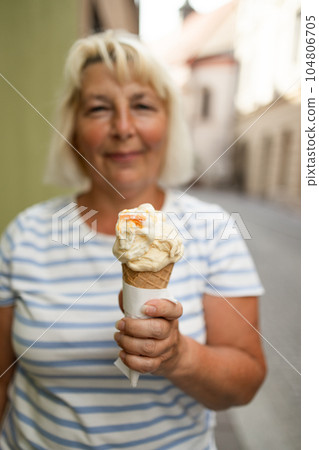 Happy 60s woman with delicious ice cream in waffle cone outdoors. Space for text 104806705