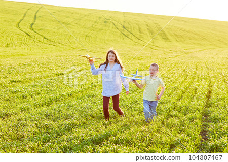 Cheerful and happy children play in the field and imagine themselves to be pilots on a sunny summer day. Kids dreams of flying and aviation. Cheerful and happy children play in the field and imagine themselves to be pilots on a sunny summer day. Kids dreams of flying and aviation. 104807467