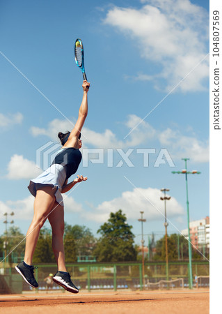 Concentrated female tennis player in motion during game, raining, playing tennis at open air court on sunny day Concentrated female tennis player in motion during game, raining, playing tennis at open air court on sunny day 104807569