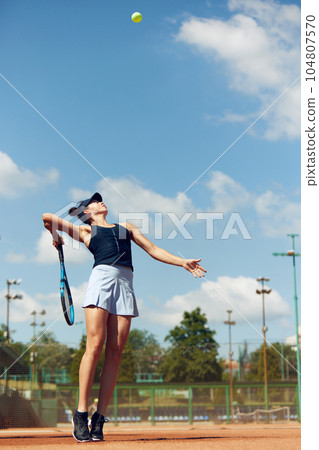 Full-length dynamic image of young athletic woman, tennis player in uniform during game, playing at open air stadium, court on warm day Full-length dynamic image of young athletic woman, tennis player in uniform during game, playing at open air stadium, court on warm day 104807570