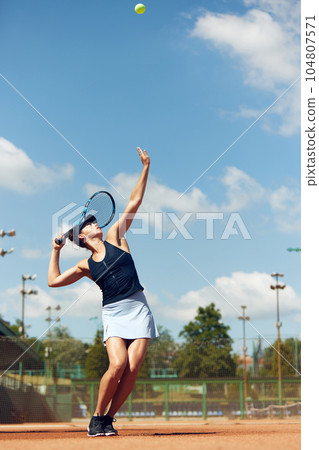 Full-length dynamic image of young athletic woman, tennis player in uniform during game, playing at open air stadium, court on warm day Full-length dynamic image of young athletic woman, tennis player in uniform during game, playing at open air stadium, court on warm day 104807571