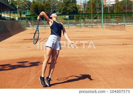 Concentrated female tennis player in motion during game, raining, playing tennis at open air court on sunny day 104807573