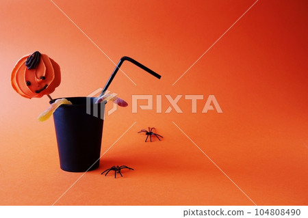 Halloween holiday concept. Black paper cup with a straw and spiders on an orange background. Copy space for your text. Halloween holiday concept. Black paper cup with a straw and spiders on an orange background. Copy space for your text. 104808490