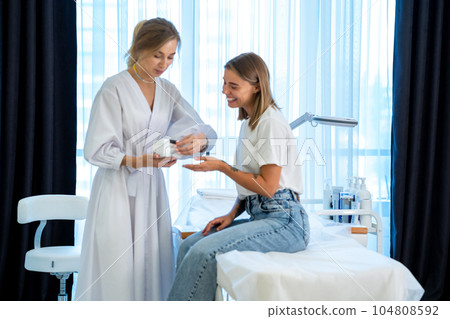 Woman cosmetologist talking to woman before procedure in esthetic cosmetology clinic. Woman cosmetologist talking to woman before procedure in esthetic cosmetology clinic. 104808592