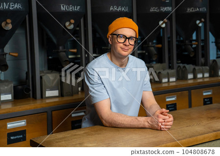 Friendly bartender in the interior of modern coffee shop with big variety of coffee beans. Friendly bartender in the interior of modern coffee shop with big variety of coffee beans. 104808678