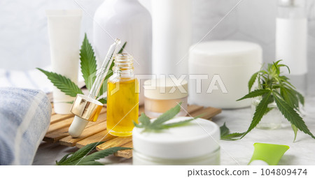 Dropper bottle with CBD oil and cream bottles green cannabis leaves close up 104809474