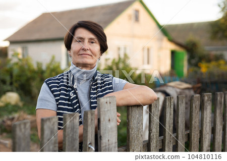 Portrait of an elderly woman at the fence of her farm on summer evening 104810116