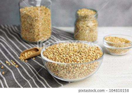 Uncooked green buckwheat grains in bowl on white wooden table 104810158