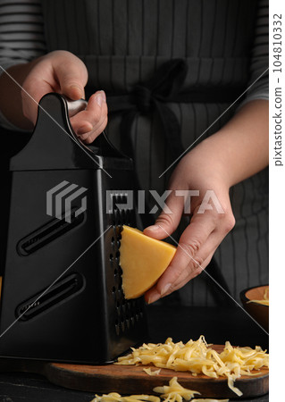 Woman grating fresh cheese at black table, closeup 104810332