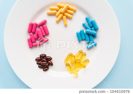 Food supplements of bright color lie on a white plate on a blue background. Concept of health support and lack of vitamins. Food supplements of bright color lie on a white plate on a blue background. Concept of health support and lack of vitamins. 104810976