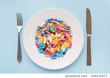 Many multi-colored bright vitamins lie on a plate along with a knife and fork. The concept of healthcare, healthy eating, diet. Many multi-colored bright vitamins lie on a plate along with a knife and fork. The concept of healthcare, healthy eating, diet. 104810977