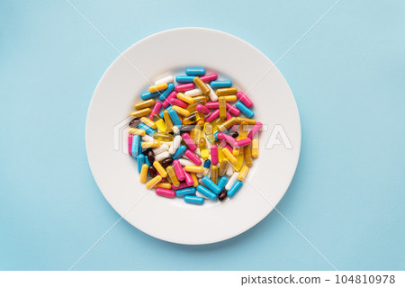 Colorful pills in a large white bowl on a blue background. The concept of health and evidence-based medicine. Place for an inscription. Colorful pills in a large white bowl on a blue background. The concept of health and evidence-based medicine. Place for an inscription. 104810978