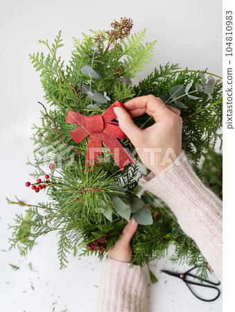 Stylish Christmas wreath for the interior, hang the wreath on the door. Handmade, the girl is holding a freshly made wreath with a beautiful red bow. Festive atmosphere. Stylish Christmas wreath for the interior, hang the wreath on the door. Handmade, the girl is holding a freshly made wreath with a beautiful red bow. Festive atmosphere. 104810983