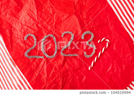 Lettering 2023 from glittering garland rain on red gift wrapping paper background. New Year and Christmas decor, Christmas candy on the background. Lettering 2023 from glittering garland rain on red gift wrapping paper background. New Year and Christmas decor, Christmas candy on the background. 104810994