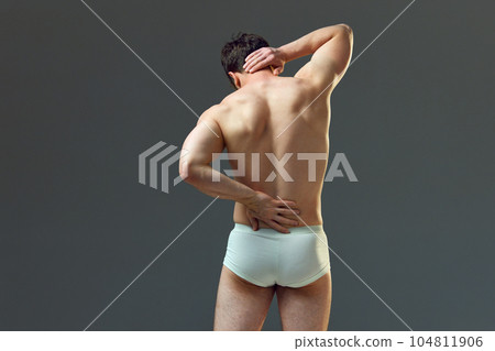 Pain in neck and spine. Cropped image of strong muscular male body, relief back. Man posing shirtless in underwear against grey studio background Pain in neck and spine. Cropped image of strong muscular male body, relief back. Man posing shirtless in underwear against grey studio background 104811906
