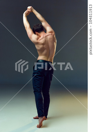 Full-length rear view image of young man with healthy, strong, muscular body, back posing shirtless in pants against grey studio background Full-length rear view image of young man with healthy, strong, muscular body, back posing shirtless in pants against grey studio background 104811913