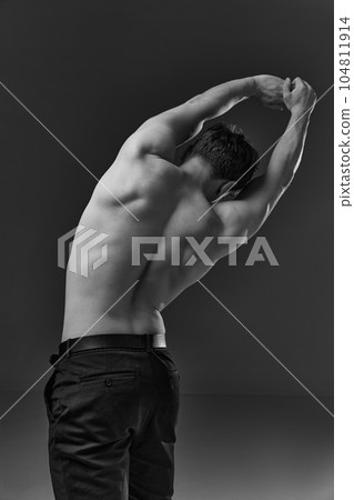 Rear view image of young man with healthy, strong, muscular body, back posing shirtless in pants. Black and white photography Rear view image of young man with healthy, strong, muscular body, back posing shirtless in pants. Black and white photography 104811914