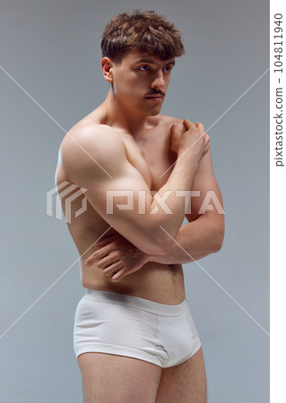 Handsome young man with muscular body posing shirtless in underwear against grey studio background. Relief hands 104811940