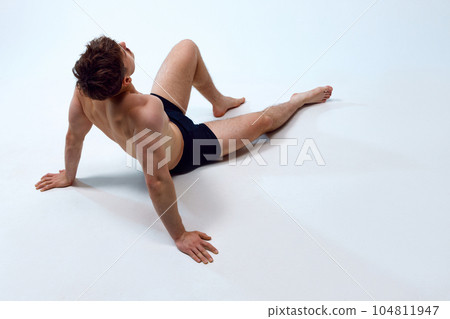 Young man with athletic, muscular, fit body lying on floor, posing shirtless in underwear against white studio background 104811947