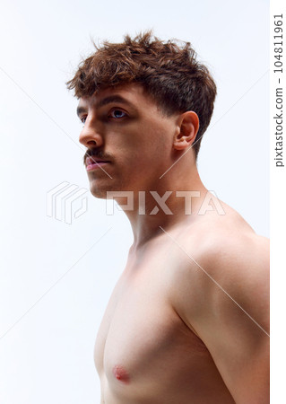 Portrait of young handsome man posing shirtless with serious facial expression against grey studio background. Muscular body Portrait of young handsome man posing shirtless with serious facial expression against grey studio background. Muscular body 104811961