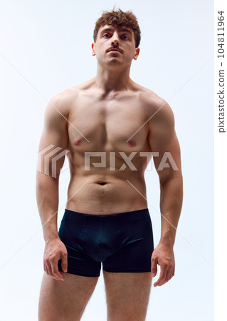 Portrait of handsome young man with mustache, posing shirtless in underwear against grey studio background. Muscular, sportive body 104811964