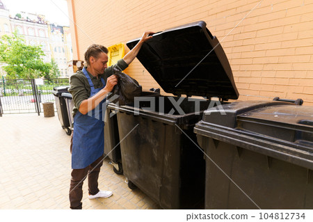 Waiter or kitchen worker responsibly disposing of garbage in pocket and placing it in city trash bin located in back yard. Focus on maintaining cleanliness and proper waste management in urban Waiter or kitchen worker responsibly disposing of garbage in pocket and placing it in city trash bin located in back yard. Focus on maintaining cleanliness and proper waste management in urban 104812734