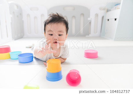 A happy 8-month-old baby playing with an educational toy on a play mat in the living room with natural light A happy 8-month-old baby playing with an educational toy on a play mat in the living room with natural light 104812737