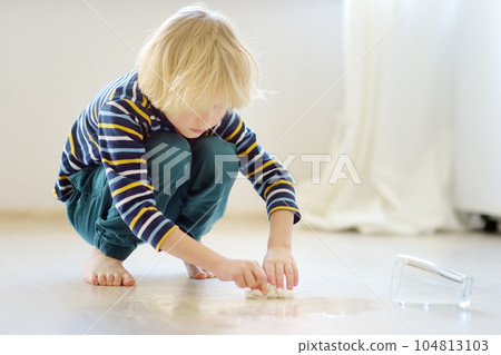 Little boy wipes water spilled from a glass on the floor. Teaching a child to clean up after himself. Responsibility, accuracy. Help around the house. Household duties. Little boy wipes water spilled from a glass on the floor. Teaching a child to clean up after himself. Responsibility, accuracy. Help around the house. Household duties. 104813103