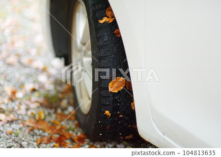 White automobile is in the mountains on autumn day. Wheel of car on gravel road with fallen leaves stuck to it. Road trip in european Alps. Travel and tourism. 104813635