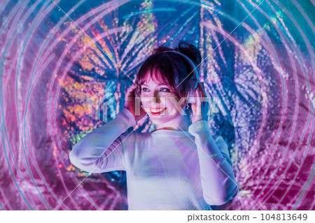 Portrait of relaxed smiling woman in white clothes and headphones dancing in neon light. Music lover. White dress code party. Silent disco. Enjoy moment on shiny background. Selective focus. Portrait of relaxed smiling woman in white clothes and headphones dancing in neon light. Music lover. White dress code party. Silent disco. Enjoy moment on shiny background. Selective focus. 104813649