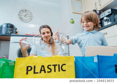 Mother is teaching kid how to recycle help the boy aware environmental importance - mom educates son sort garbage into different bins on kitchen. Family sorting garbage at home. Concept of recycling. Mother is teaching kid how to recycle help the boy aware environmental importance - mom educates son sort garbage into different bins on kitchen. Family sorting garbage at home. Concept of recycling. 104813655