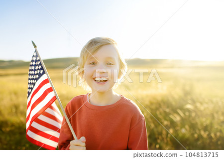 Cute little boy celebrating of July, 4 Independence Day of USA at sunny summer sunset. Child running with american flag of United States on wheat field. Proud small american boy holding country flag Cute little boy celebrating of July, 4 Independence Day of USA at sunny summer sunset. Child running with american flag of United States on wheat field. Proud small american boy holding country flag 104813715