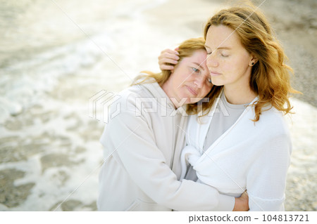 Redhead senior mother and her beautiful adult daughter are walking together and embracing. Family relationships between adult children and older parents 104813721