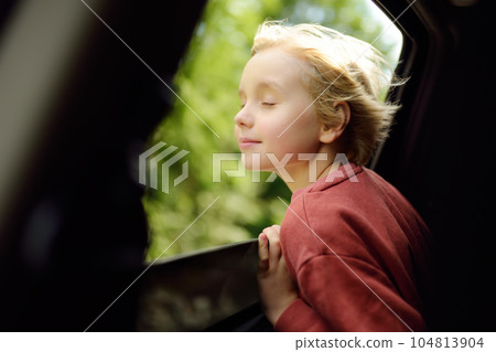 Cute preteen boy inhales the air of freedom from car window during family road trip and enjoy of pleasant expectation of happy vacation. Joyful child travel with parents Cute preteen boy inhales the air of freedom from car window during family road trip and enjoy of pleasant expectation of happy vacation. Joyful child travel with parents 104813904