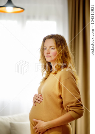 Pregnant caucasian woman relaxing at home. Young expectant mother strokes her pregnant belly and thinks about the baby childbirth. Concept of motherhood and pregnancy Pregnant caucasian woman relaxing at home. Young expectant mother strokes her pregnant belly and thinks about the baby childbirth. Concept of motherhood and pregnancy 104813922