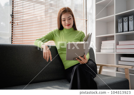 Asian young woman making notes in paper notebook sitting on cozy sofa on background of window. Pretty female writing notes in diary or making to do list relaxing at home Asian young woman making notes in paper notebook sitting on cozy sofa on background of window. Pretty female writing notes in diary or making to do list relaxing at home 104813923