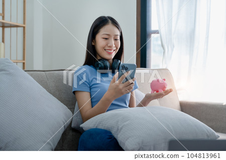 Asian young woman holding a piggy bank and using smartphone mobile, Savings concepts 104813961