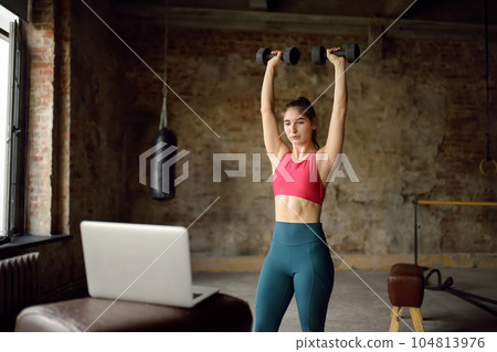 Girl trainer leads online fitness class.Young woman doing workout by laptop. Regular sports boosts immune system and promote good health and resistance to diseases. 104813976