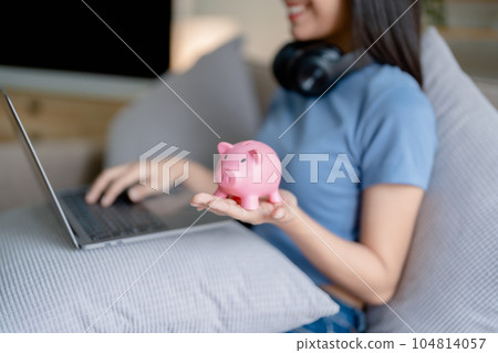 Asian young woman holding a piggy bank and using computer, Savings concepts Asian young woman holding a piggy bank and using computer, Savings concepts 104814057