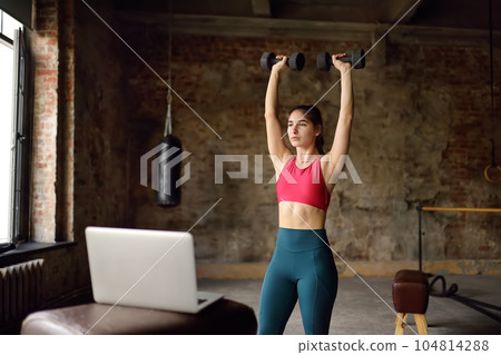 Girl trainer leads online fitness class.Young woman doing workout by laptop. Regular sports boosts immune system and promote good health and resistance to diseases. 104814288