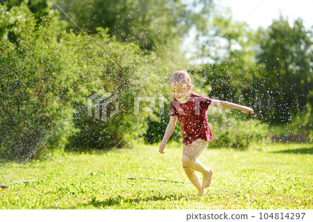 Funny little boy playing with garden sprinkler in sunny backyard. Preschooler child laughing, jumping and having fun with spray of water. Funny little boy playing with garden sprinkler in sunny backyard. Preschooler child laughing, jumping and having fun with spray of water. 104814297
