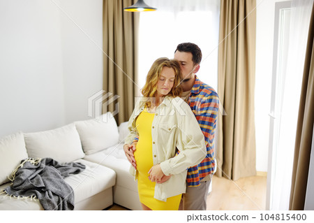 Happy young family pregnant expecting a baby dancing at home. 104815400