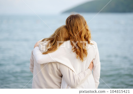 Redhead senior mother and her adult beautiful daughter are walking together on the sea shore. 104815421