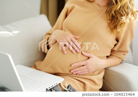 Pregnant woman works at a computer in a home office. Expectant mother searches for information on the Internet or makes online purchases of baby goods. 104815464