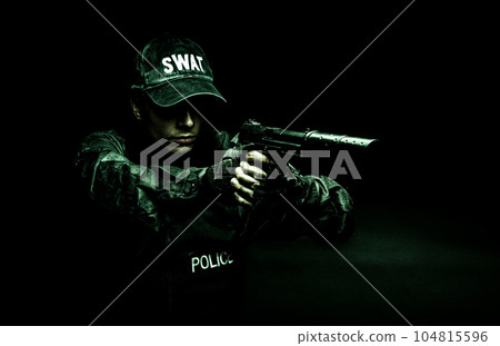 Spec ops police officer SWAT in black uniform aiming pistol with silencer, studio shot, half length 104815596