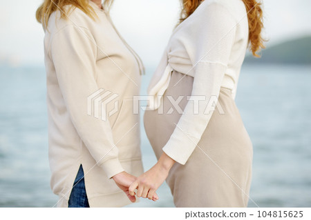 Senior mother and her adult beautiful pregnant daughter are walking together on the sea shore. A happy meeting of a mom and her grown child. 104815625