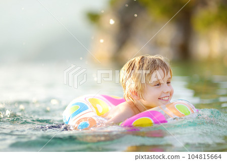 Little boy swimming with colorful floating ring in sea on sunny summer day. Cute child playing in clean water. Family and kids resort holiday during summer vacations. 104815664