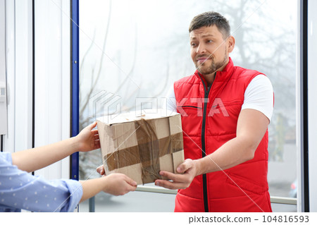 Emotional courier giving damaged cardboard box to client in doorway, closeup. Poor quality delivery 104816593