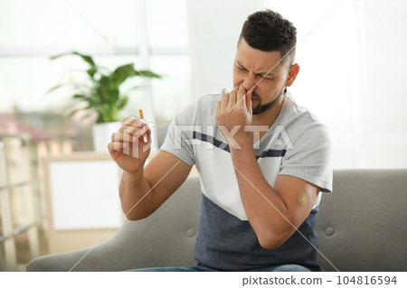 Emotional man with nicotine patch and cigarette at home 104816594